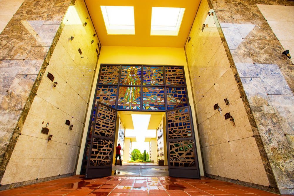 Open decorative gate leading to a sunlit courtyard with palm trees and tiled walls