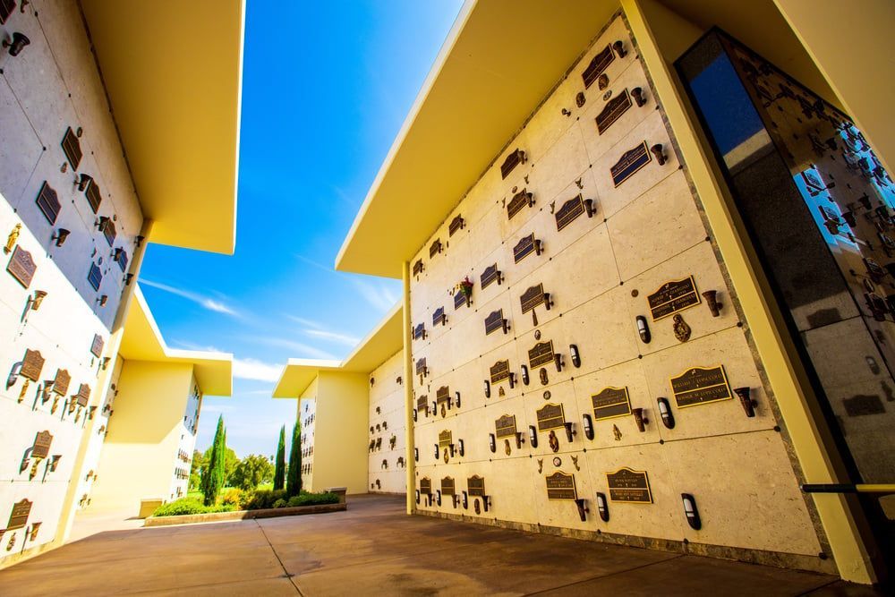 Outdoor memorial corridor with engraved walls, bright yellow overhangs, and blue sky above.