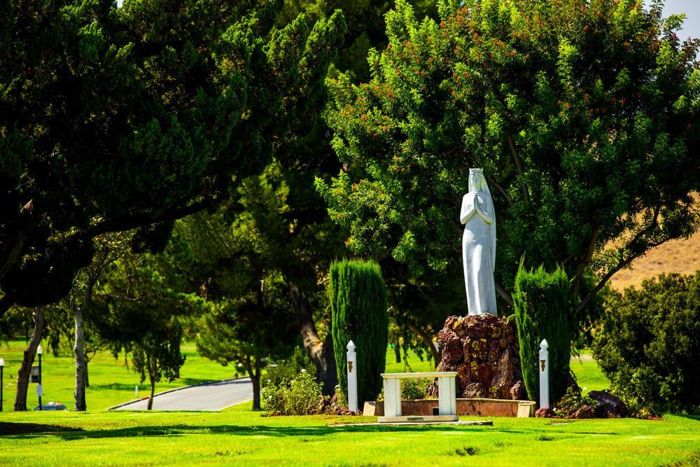 White statue on a stone pedestal in a green park with trees and bright grass