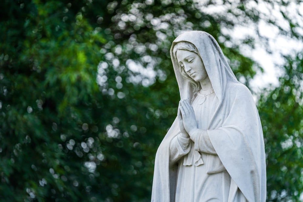 White statue of a hooded figure with folded hands in a green garden