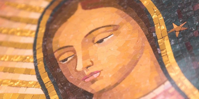 Close-up of a painted face with closed eyes in warm orange and gold tones, likely a religious mosaic