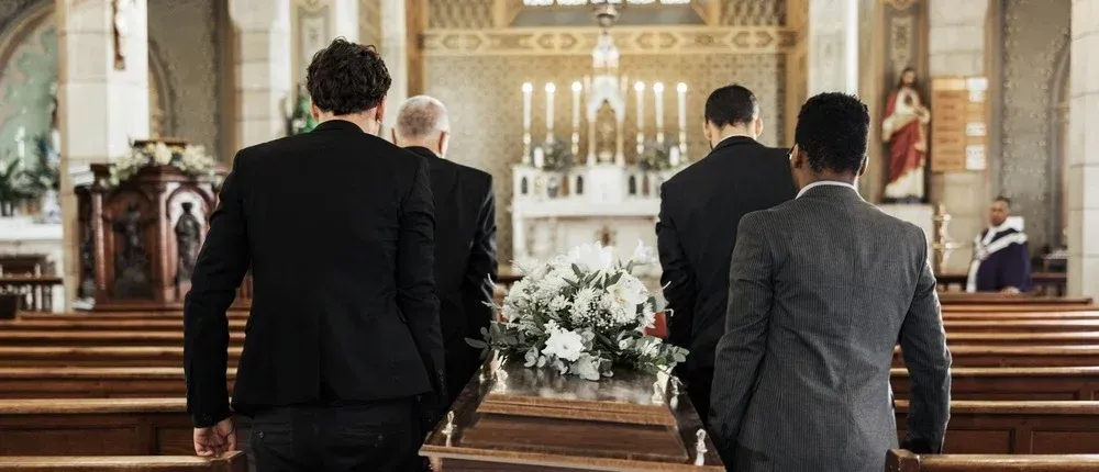 Three men in suits stand in a church facing a flower-covered altar during a wedding ceremony.