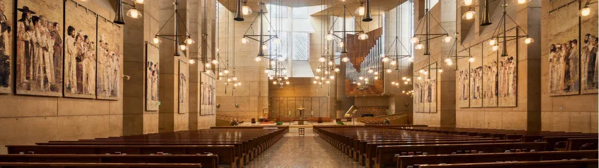 Grand church interior with wooden pews, ornate murals, and warm hanging lights