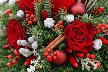 Red roses, evergreen branches, berries, cinnamon sticks, and silver ornaments in a festive holiday arrangement