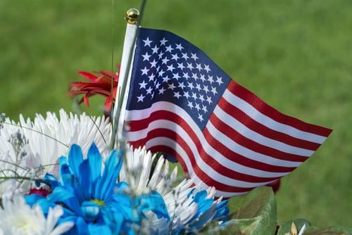 Small American flag among red, white, and blue flowers on a grassy background