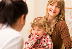 Woman smiling with a child on her lap during a conversation with another person