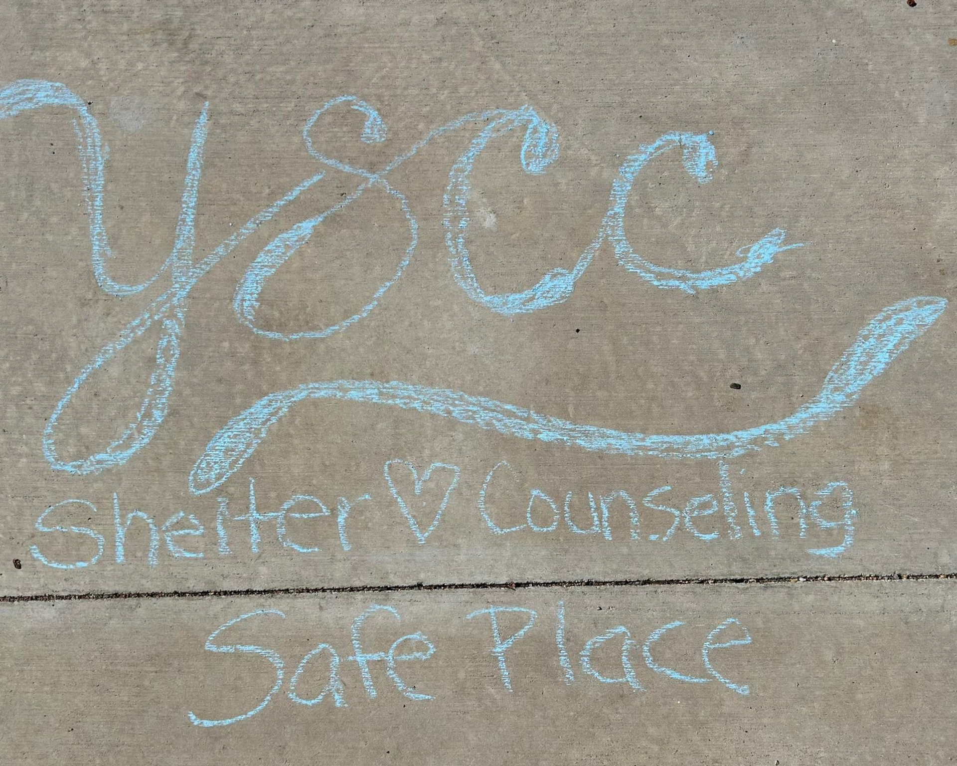 Light blue chalk writing on concrete: YCC, Shelter & Counseling, Safe Place.
