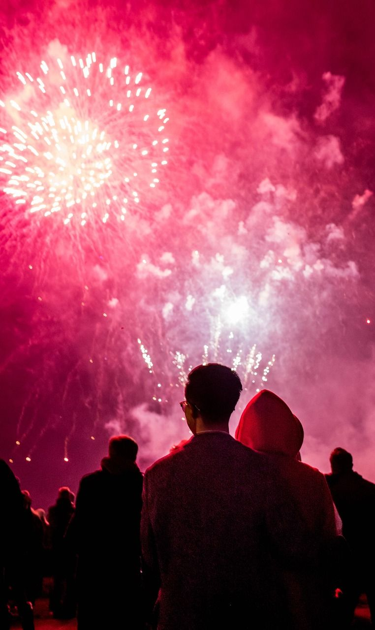 People watch red fireworks burst in the night sky.