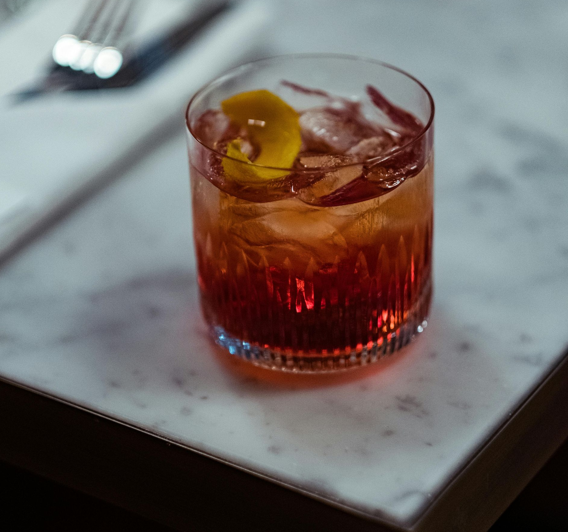 Cocktail in a glass with ice and an orange peel on a marble surface.