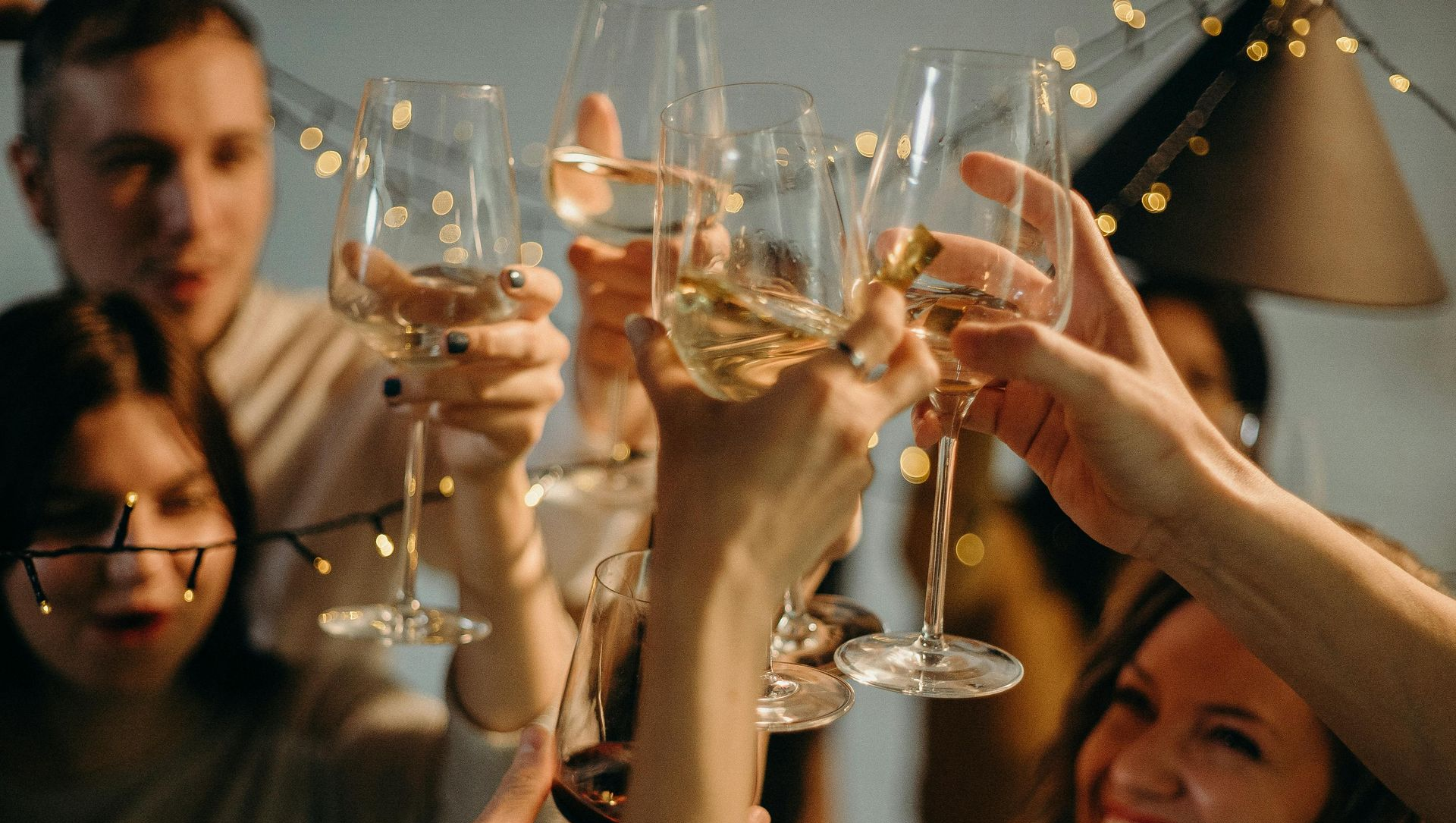 People toasting with champagne glasses at a party, illuminated by string lights.