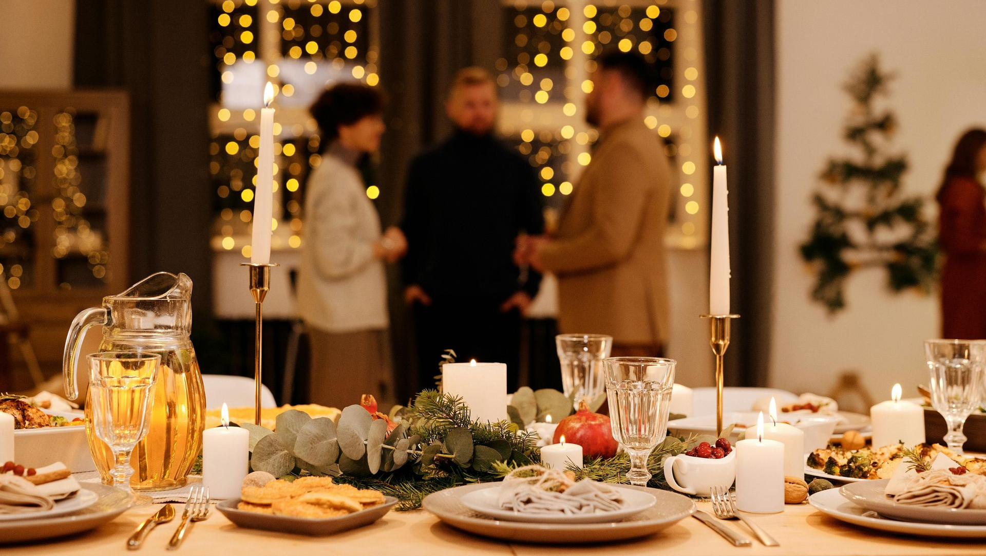 Festive dinner table set for holiday gathering with candles, food, and blurred people in background.