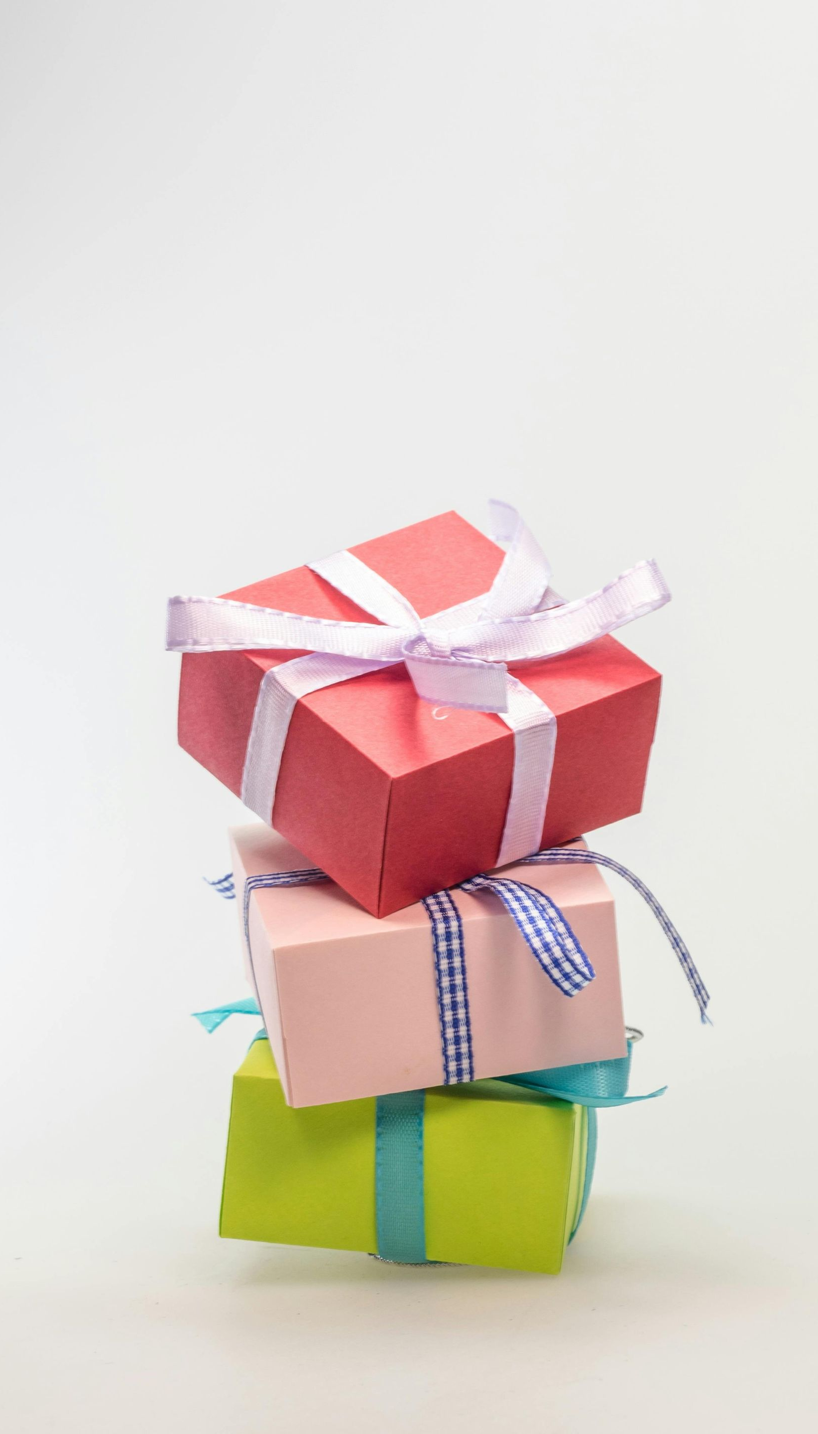 Stack of three colorful wrapped gifts with ribbons on a white background.