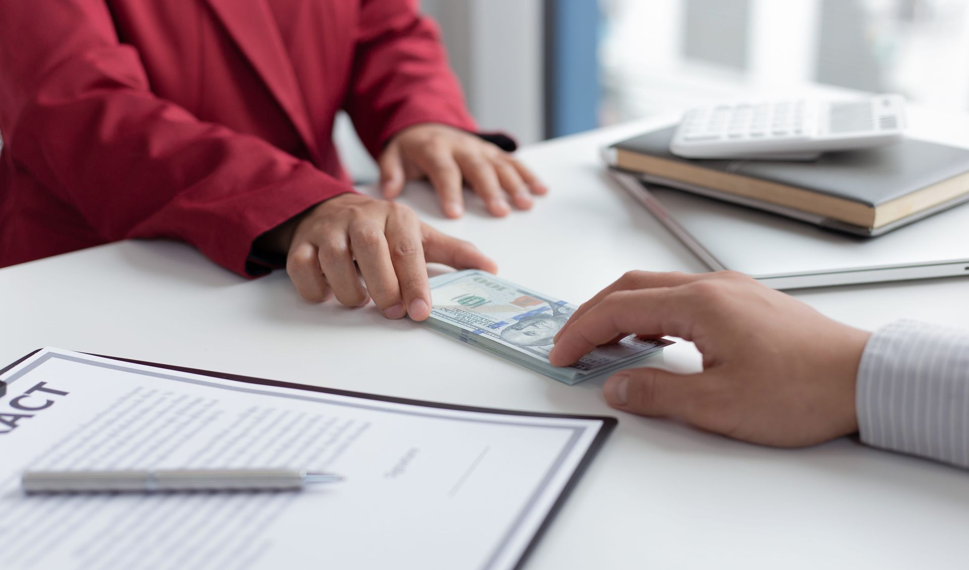 Hands exchanging cash over a desk with paperwork and a calculator