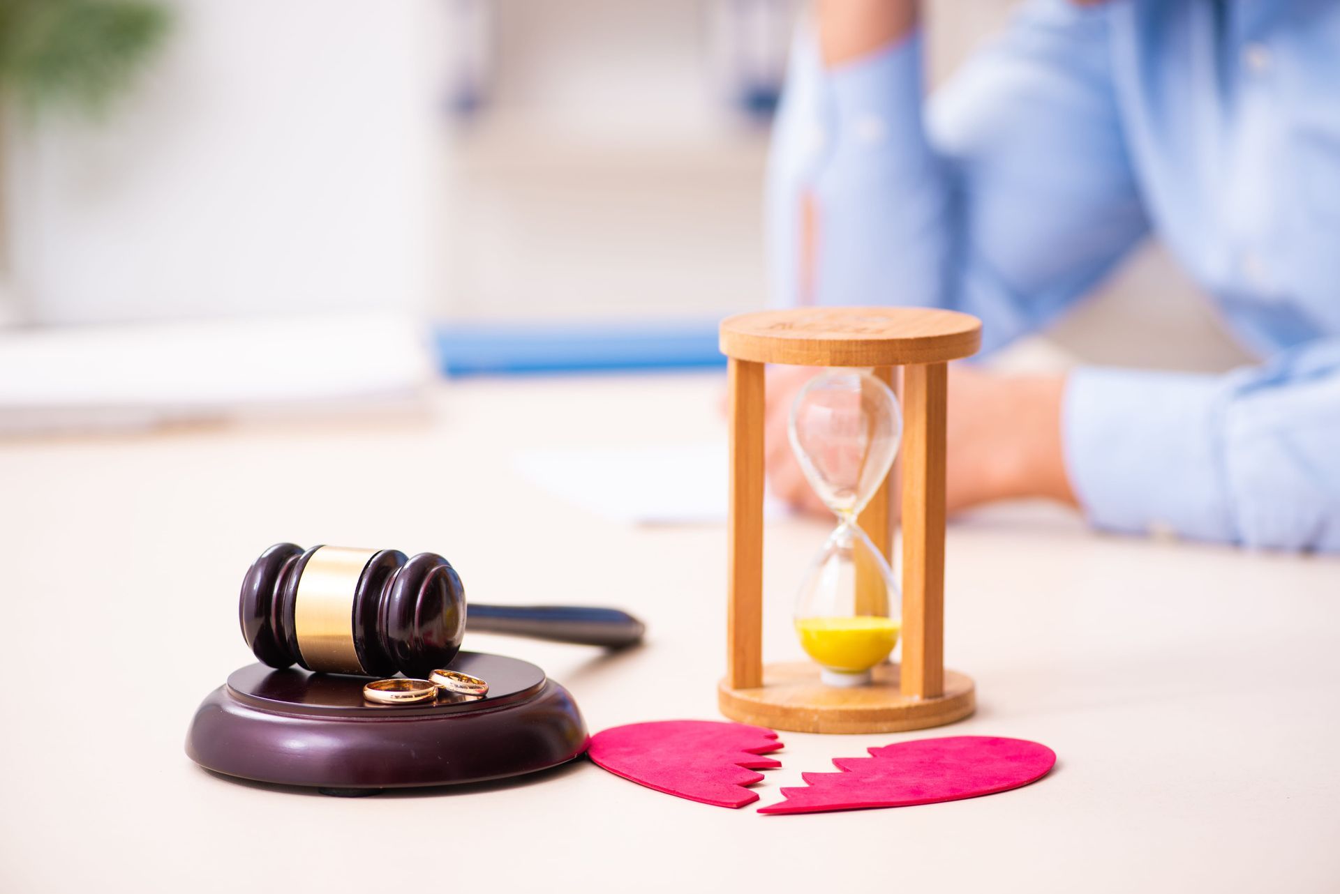 Gavel on a heart beside an hourglass, with a blurred person in the background