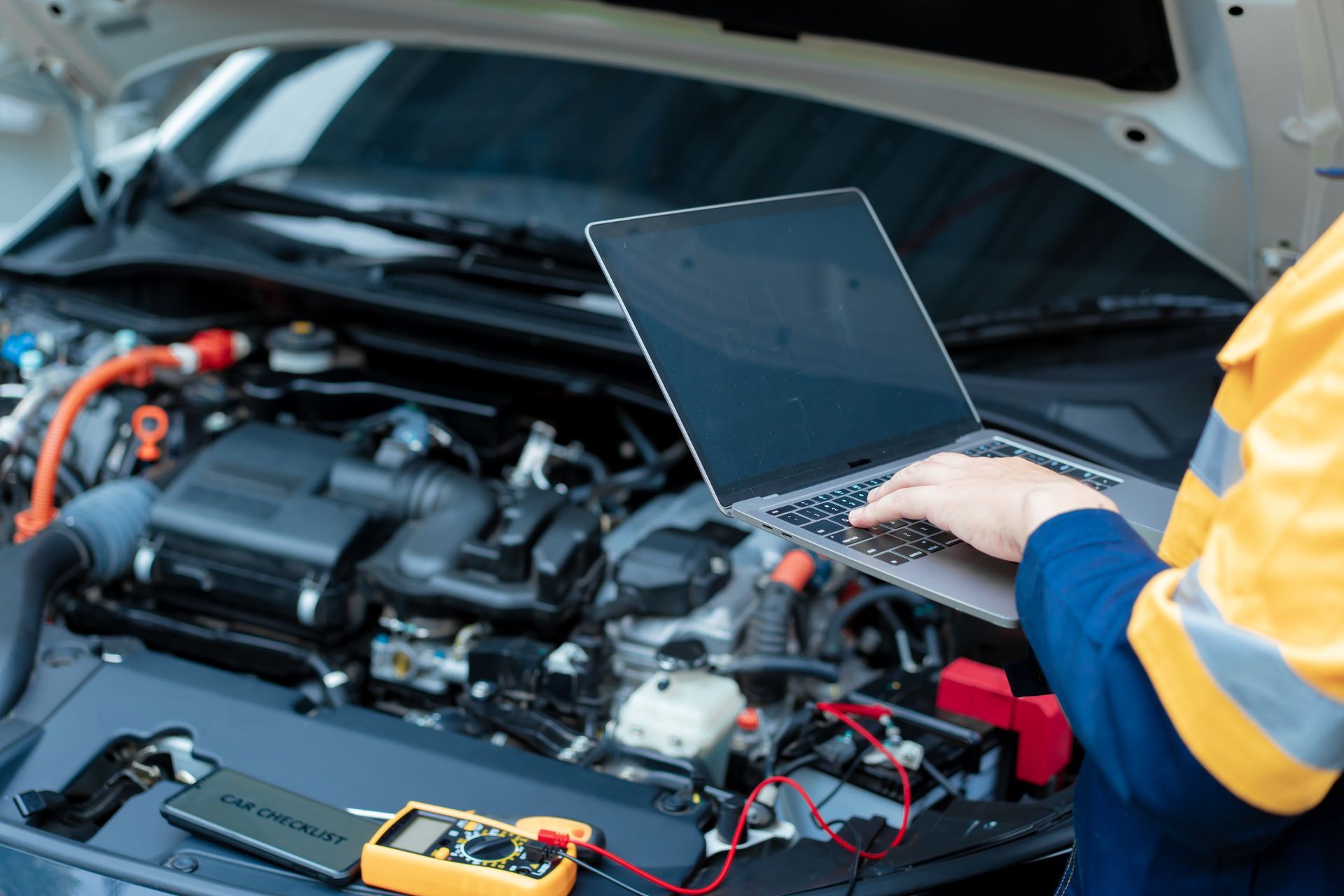Meccanico che utilizza un computer portatile per diagnosticare il motore di un'auto, con gli strumenti in primo piano.
