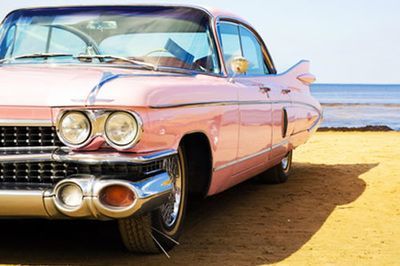 Pink classic car parked on a sandy beach.