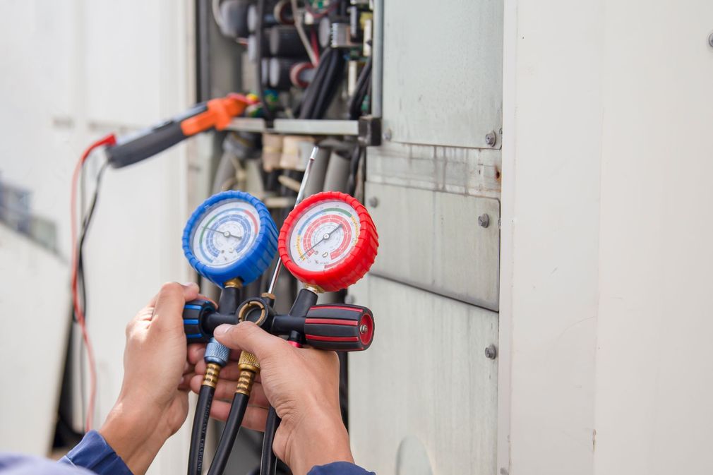 Technician using HVAC manifold gauges to service an outdoor air-conditioning unit