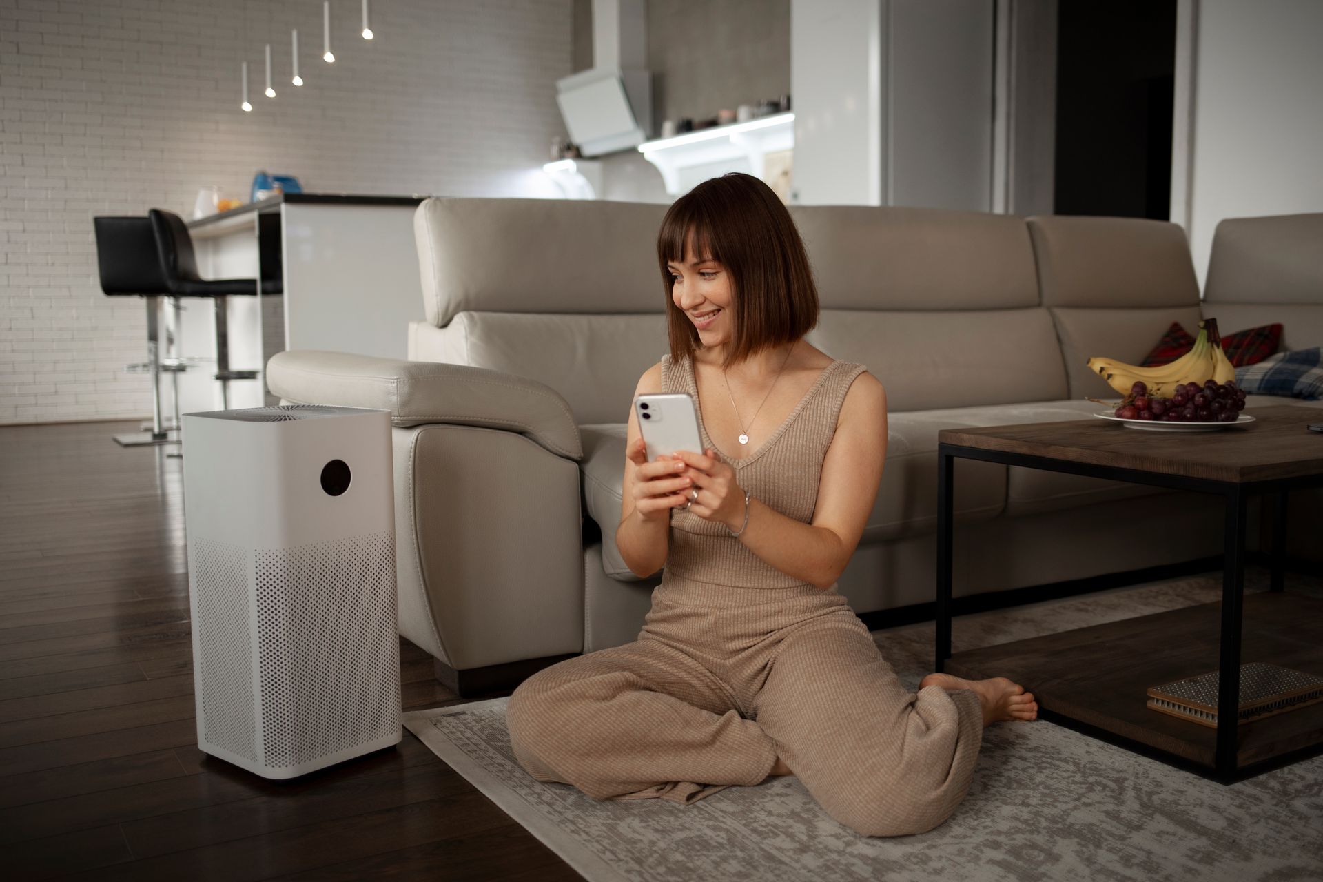 Woman sitting on a rug in a living room, looking at her phone beside a couch and coffee table.