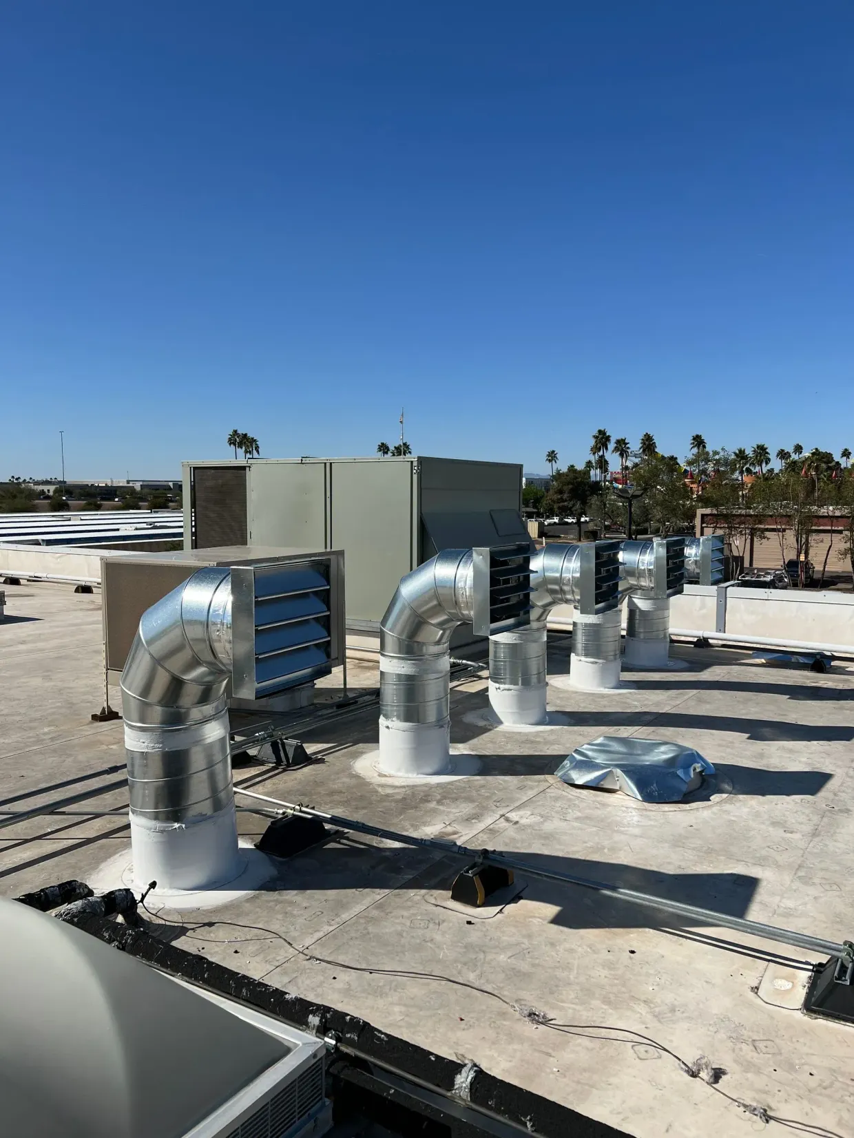 Rooftop HVAC ducts and vents under a clear blue sky, with palm trees in the distance