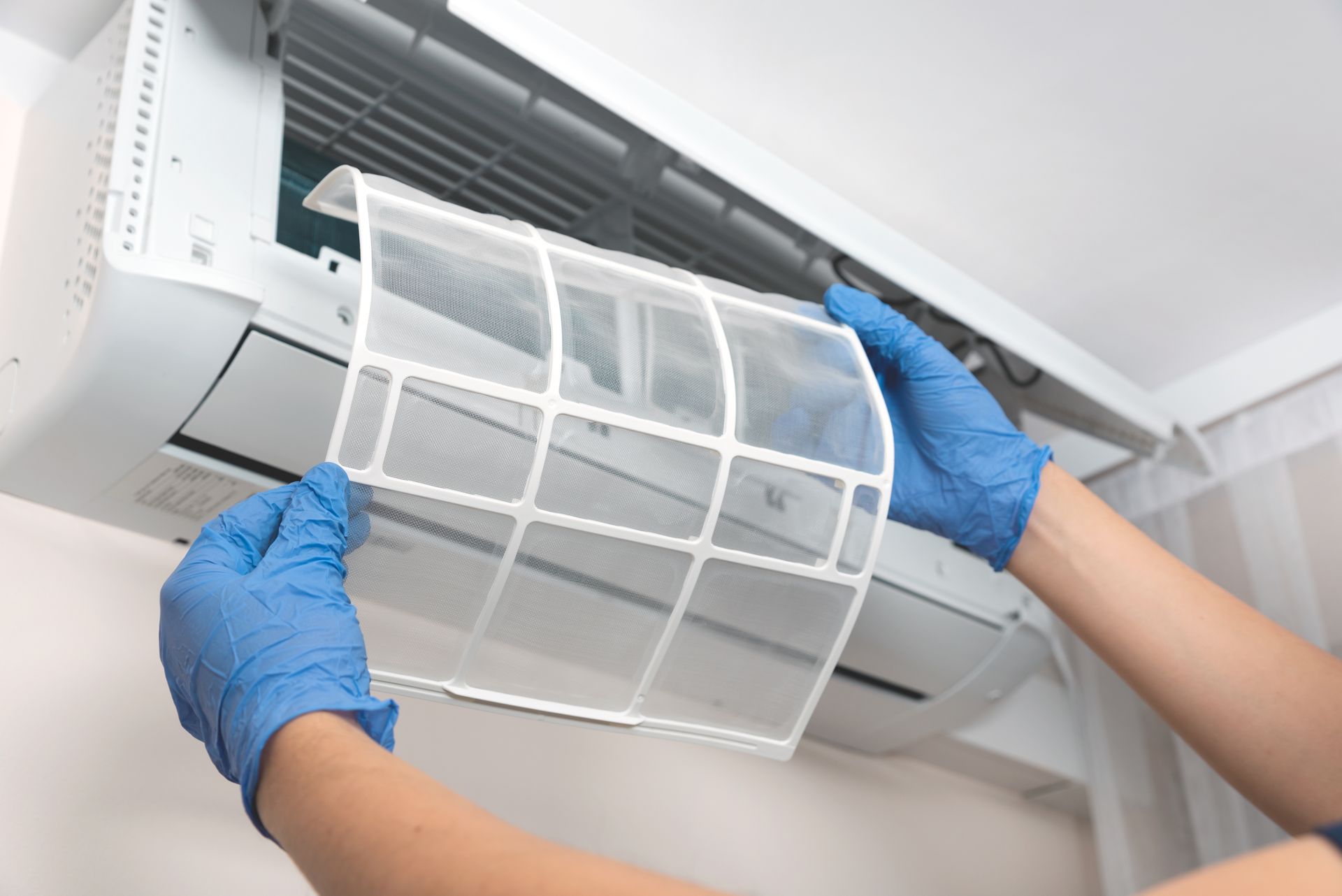 Gloved hands removing a dirty air conditioner filter for cleaning