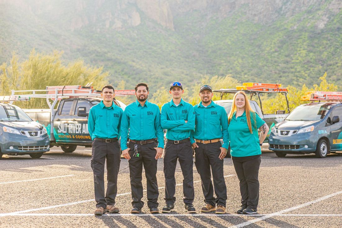 Five uniformed team members standing in front of two parked cars and a mountain backdrop