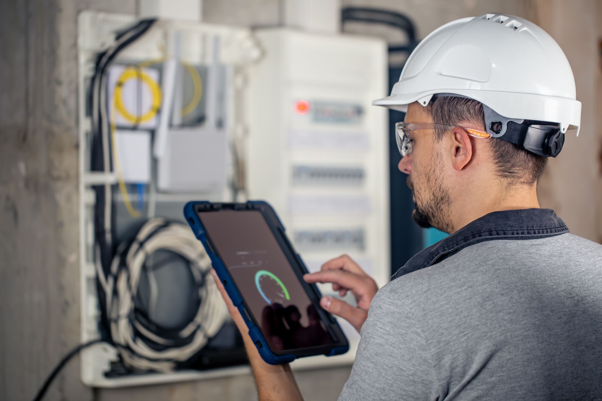 A man in a hard hat is looking at a tablet.