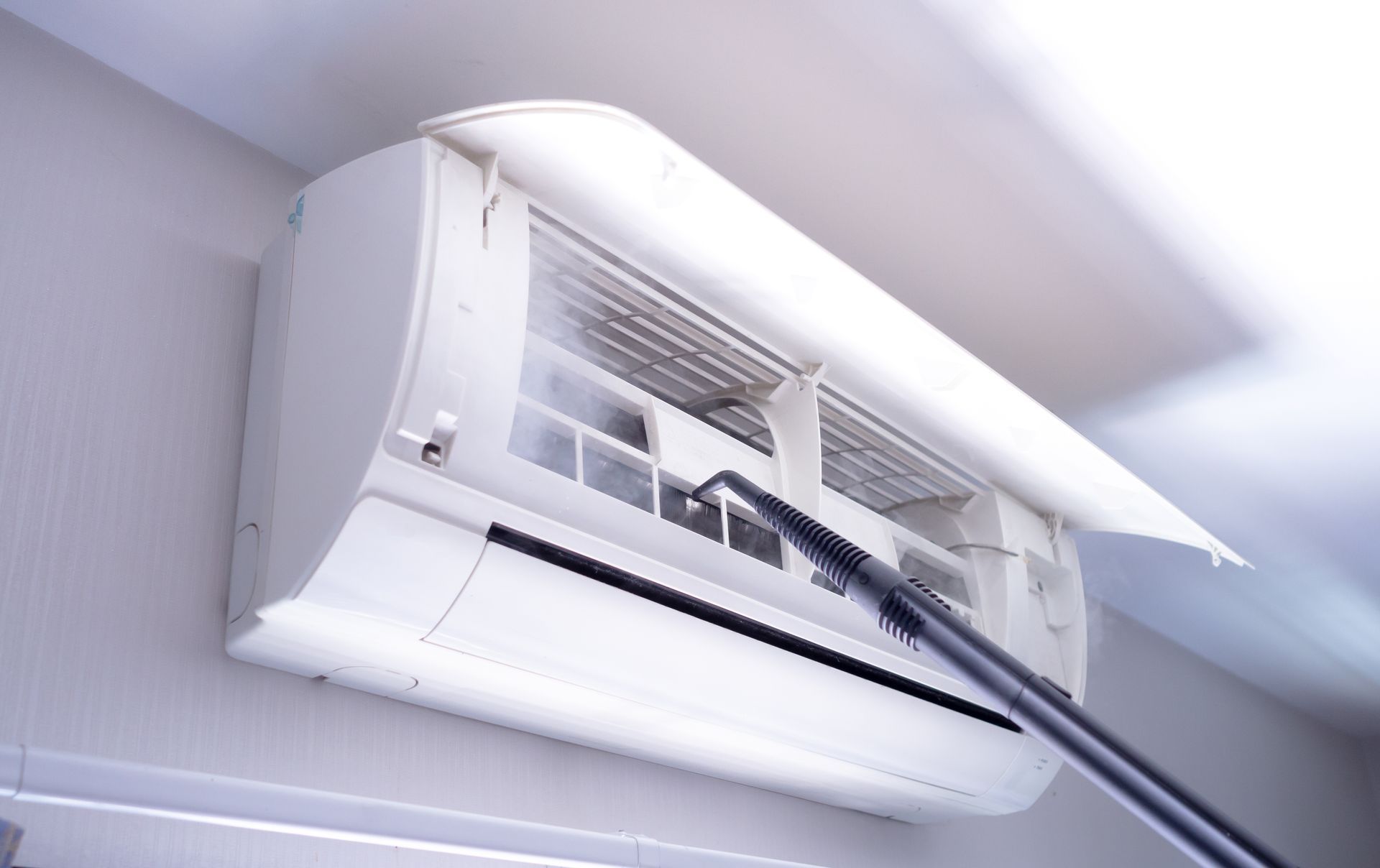 A person is cleaning an air conditioner with a vacuum cleaner.