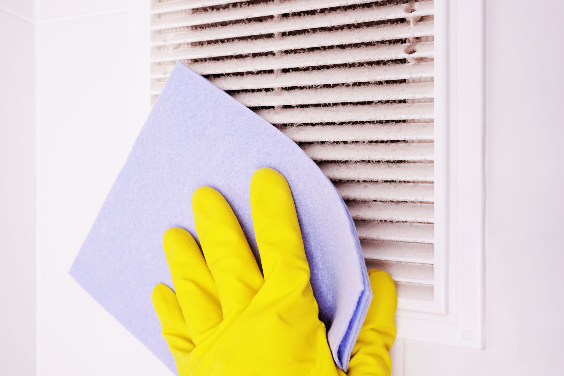 A person wearing yellow gloves is cleaning a vent with a cloth.