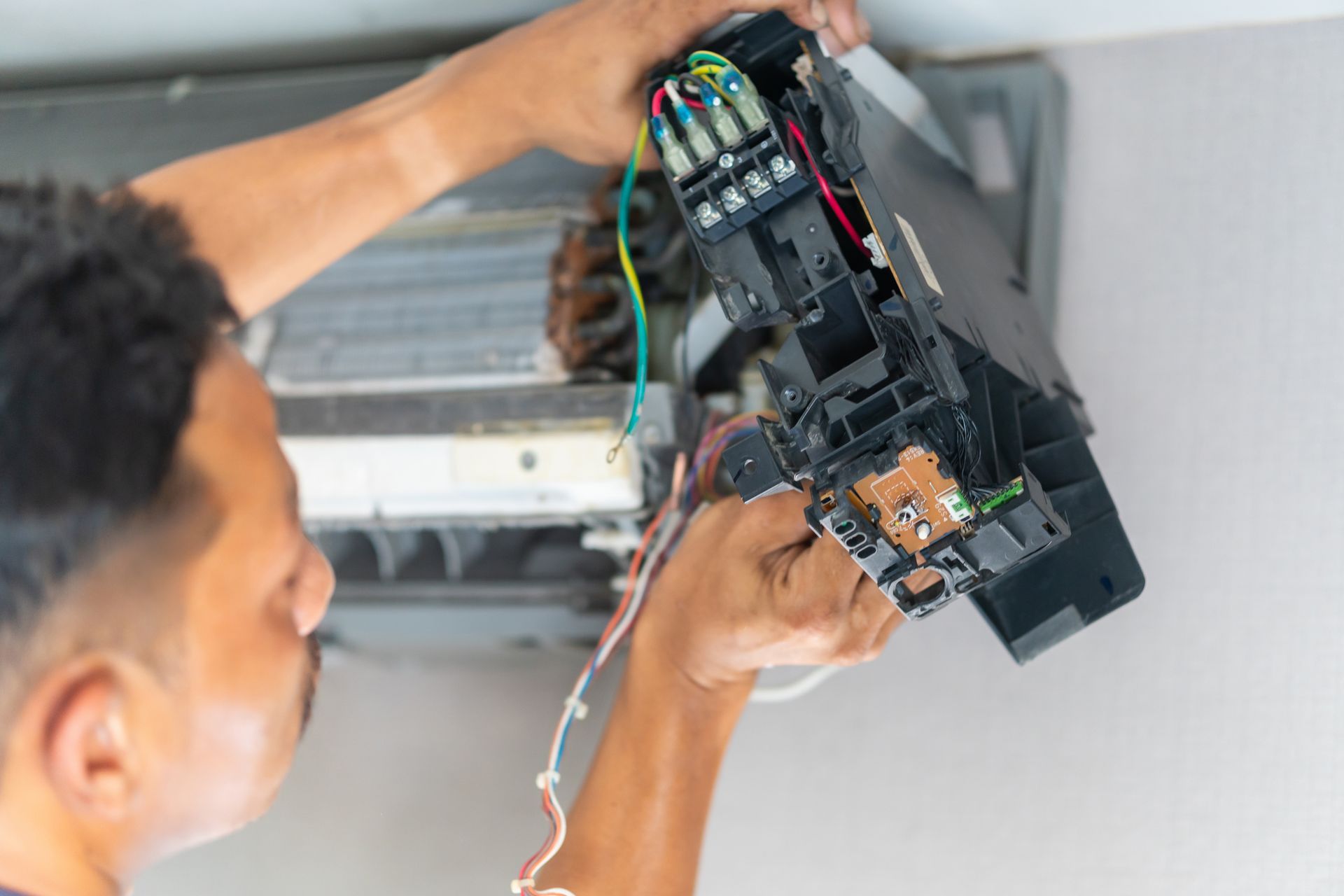 A man is fixing an air conditioner with a screwdriver.