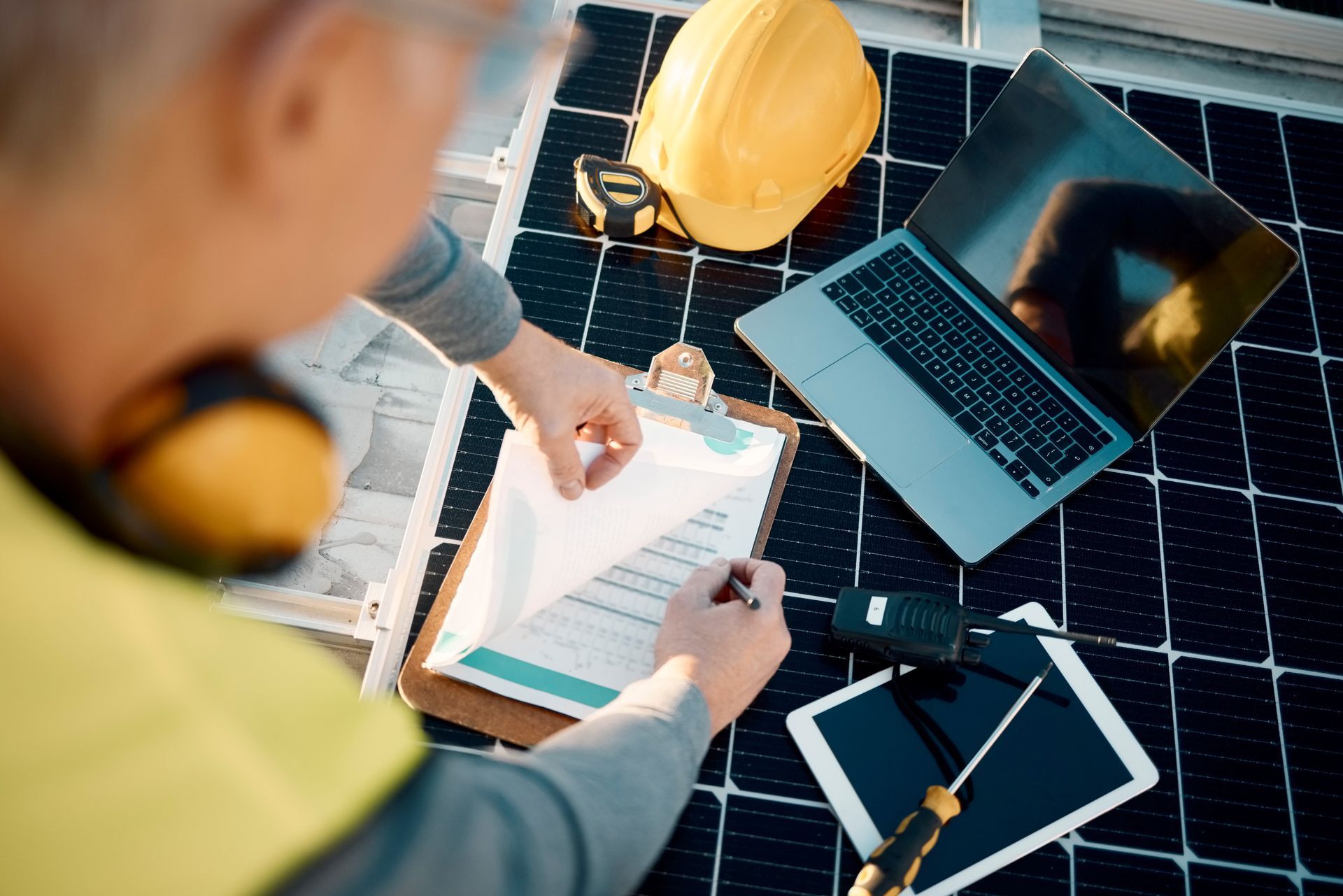 A man is working on a solar panel with a laptop and a tablet.