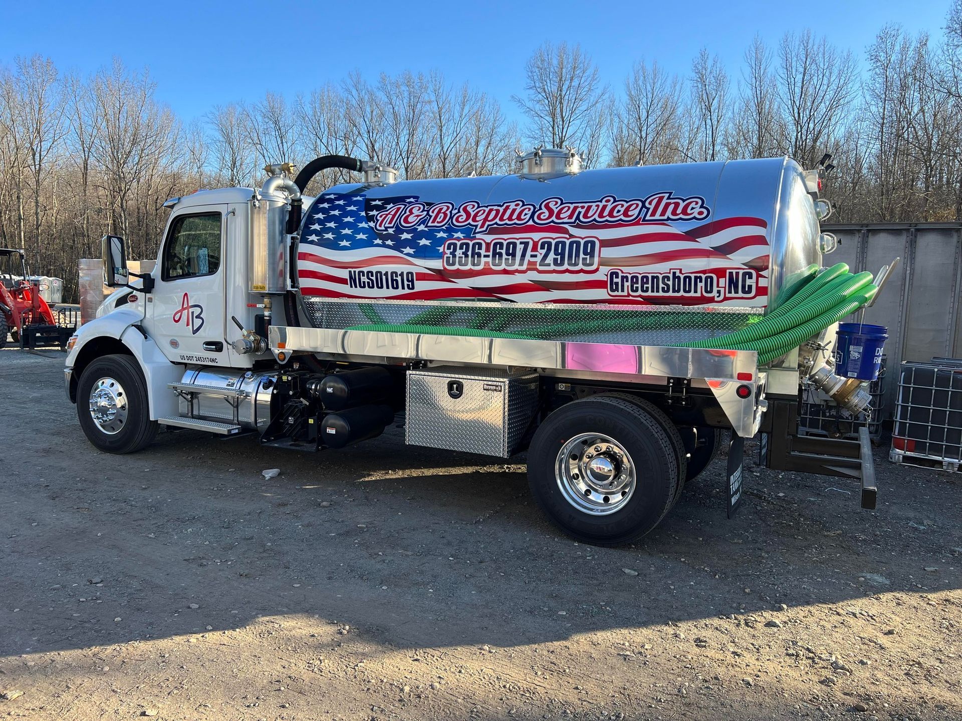 A white industrial vacuum truck with an American flag decal on the side tank, parked outdoors on a gravel lot.
