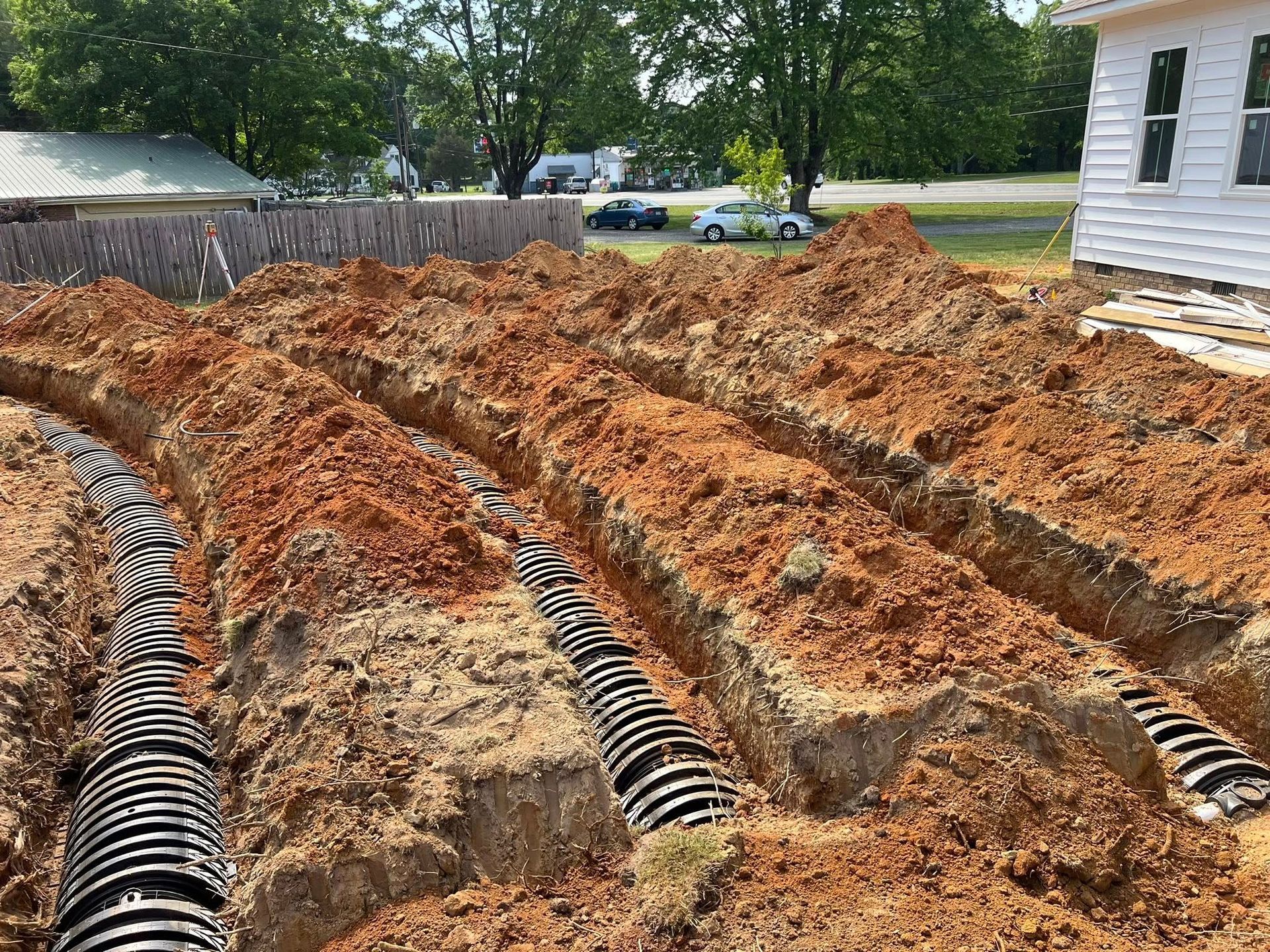 A side view of a backyard showing three long, parallel trenches containing black septic chamber drainage pipes.