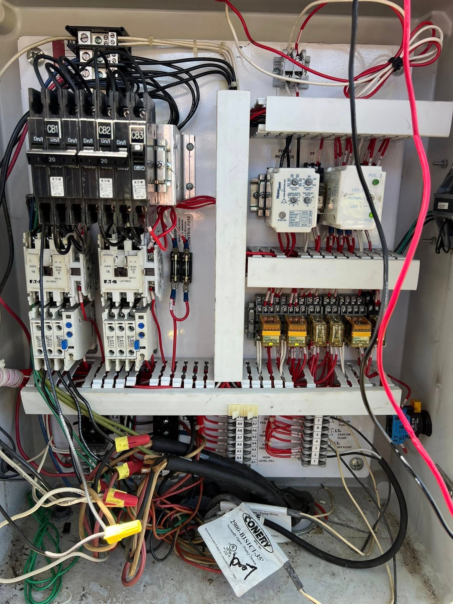 An open electrical control box with mounted circuit breakers, contactors, relays, and various colored wiring.