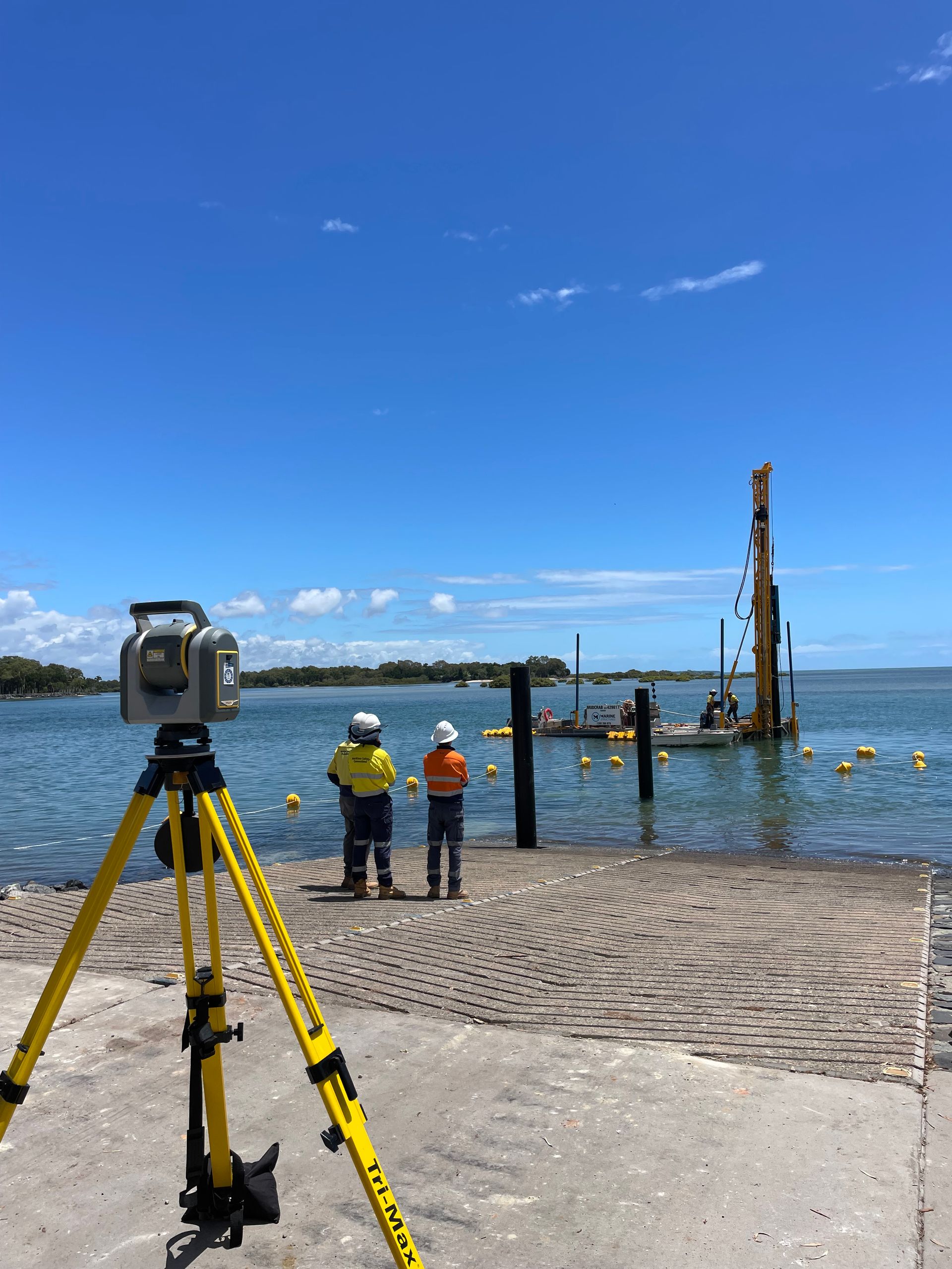 Survey equipment on a pier overlooking water, construction crew in the distance — Next Step Surveying in Aroona, QLD