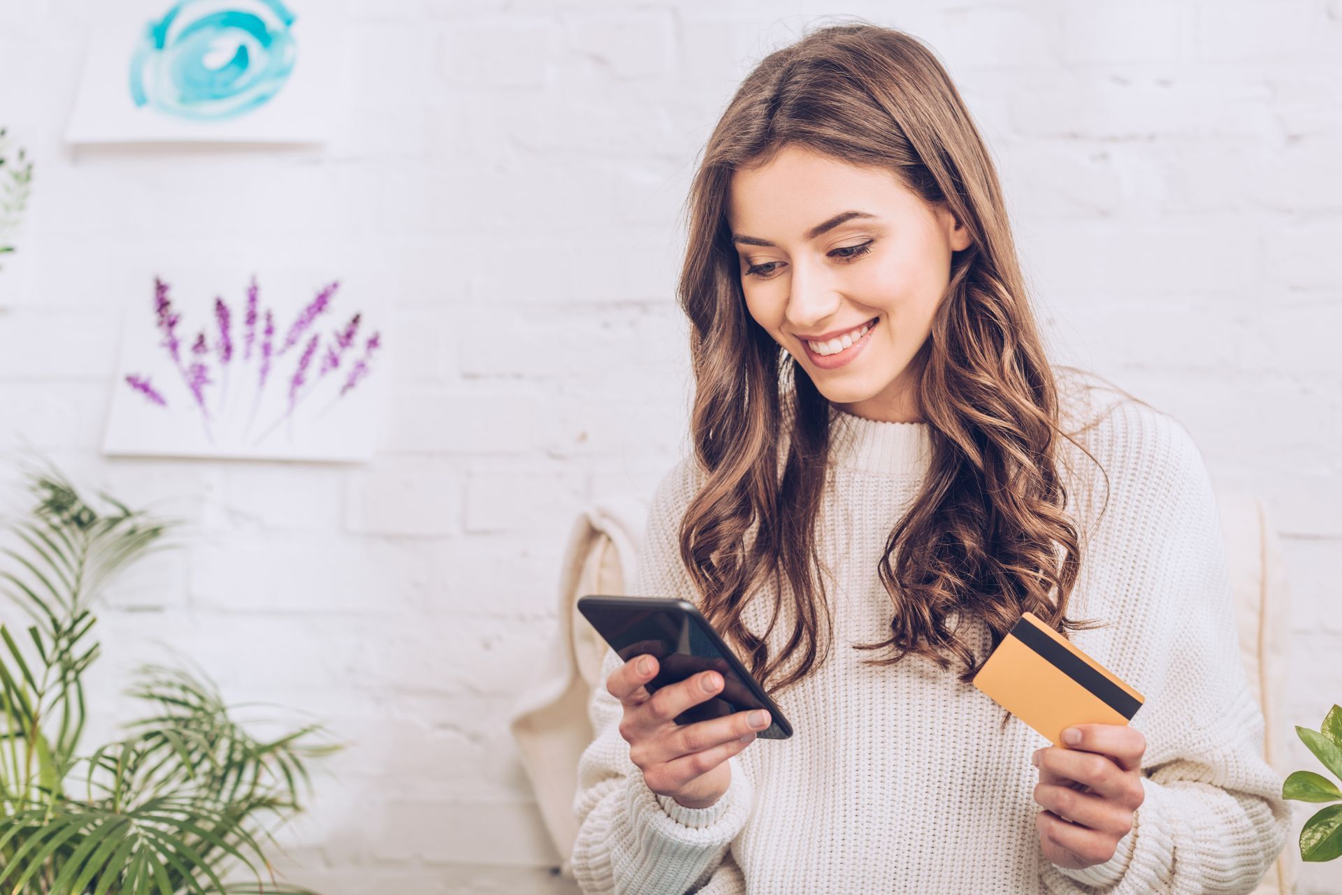 WOMAN SIGNS UP USING HER CREDIT CARD AND SMARTPHONE FOR ONLINE MEMBERSHIP OFFER Smiling woman holding a credit card and a cell phone signing up for online membership and the benefits of special offers