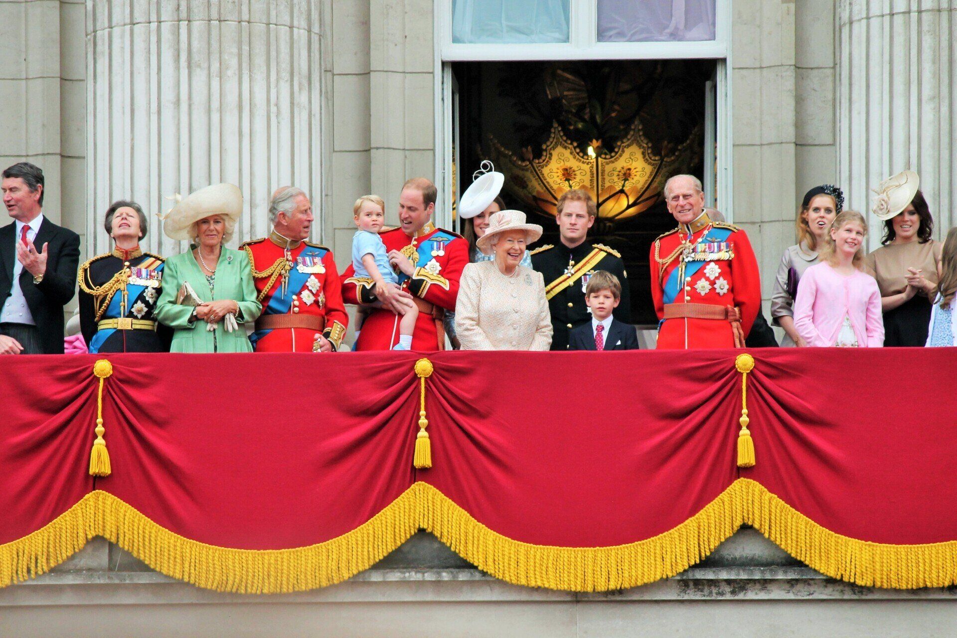 A group of people standing on a balcony with red curtains