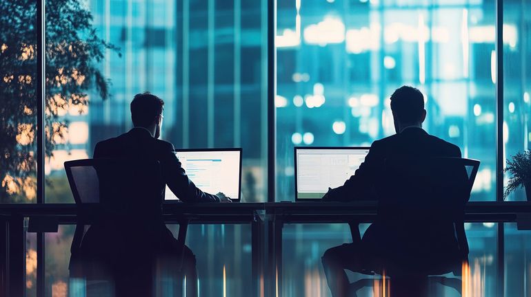 Two people managing ecommerce at workstations in a office with large windows and city lights outside.