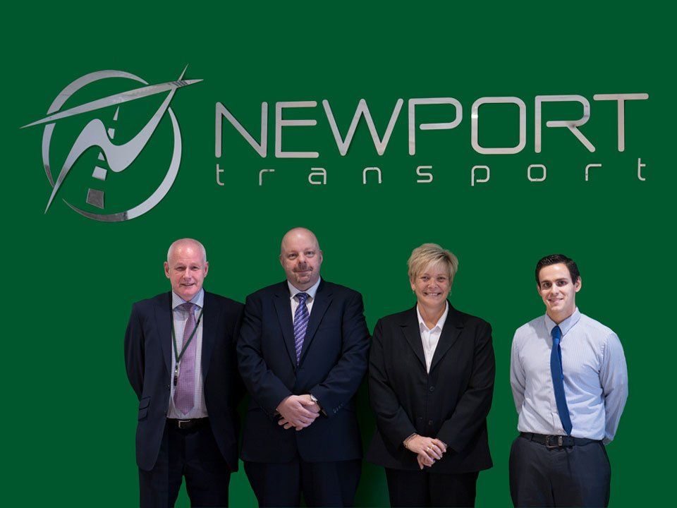 Newport Bus management team standing in front of a newport transport logo on a green background