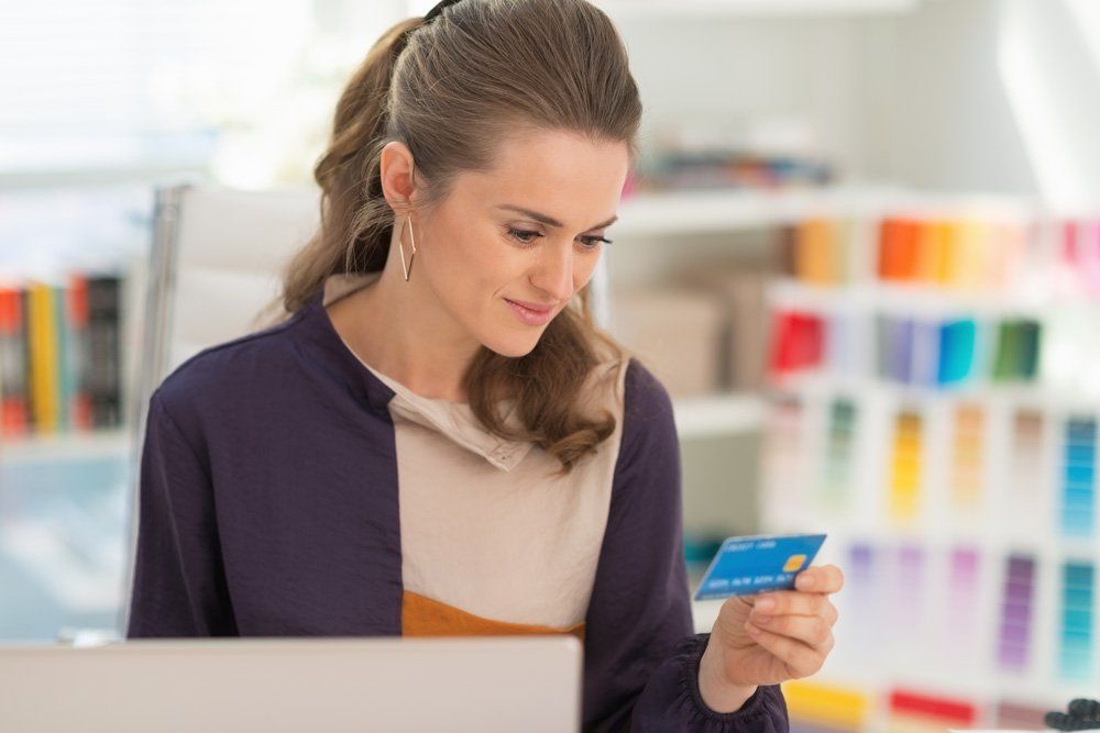A woman is holding a credit card in front of a laptop computer examining the rear 3 security digits of the card