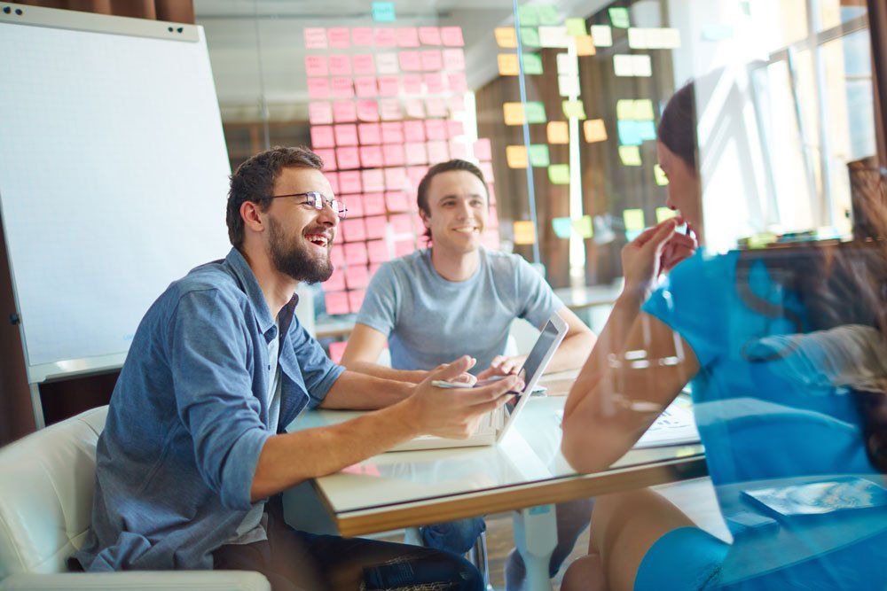 A group of people are sitting at a table with sticky notes on the wall behind them.