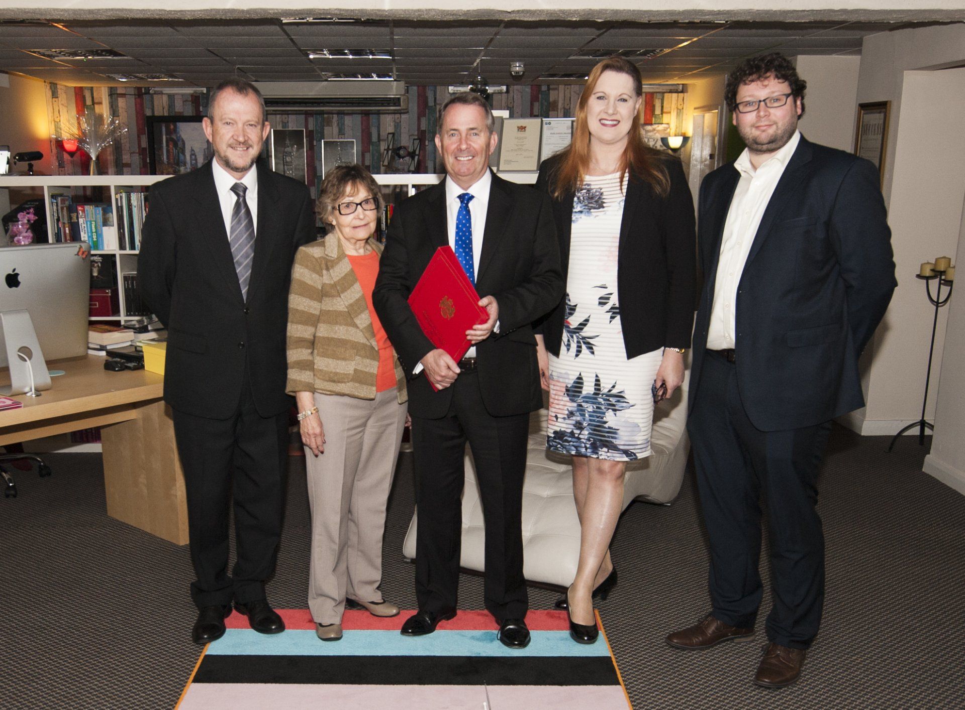 A group of staff from Trusted Xperts Limited posing for a picture with the Secretary of State for International Trade Dr Liam Fox MP holding a red ministerial book