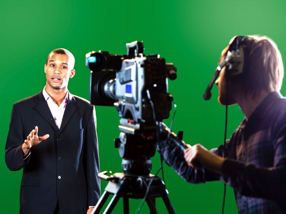 A man in a suit is talking to another man in front of a camera