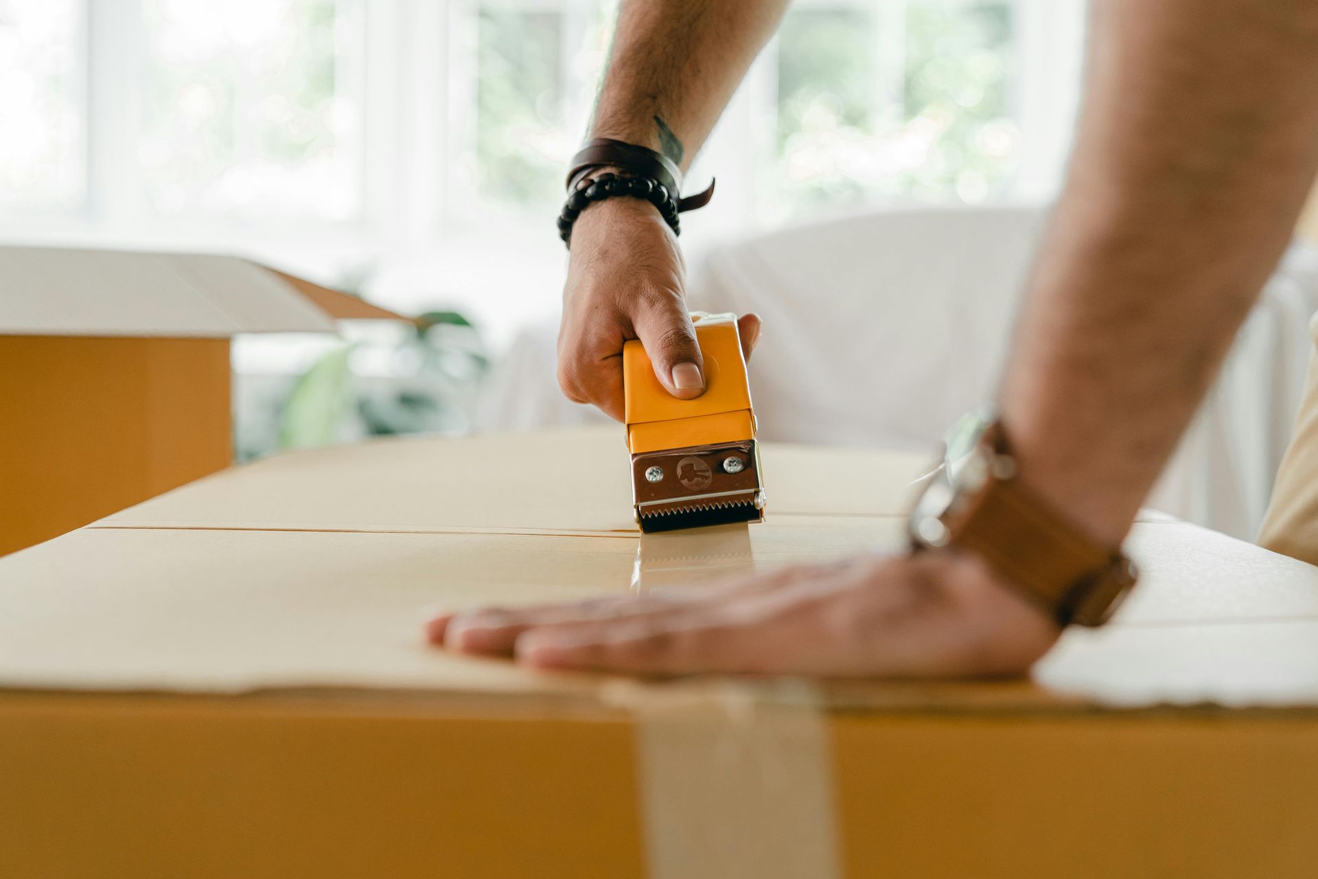 Hand using a tape dispenser to seal a cardboard box on a table