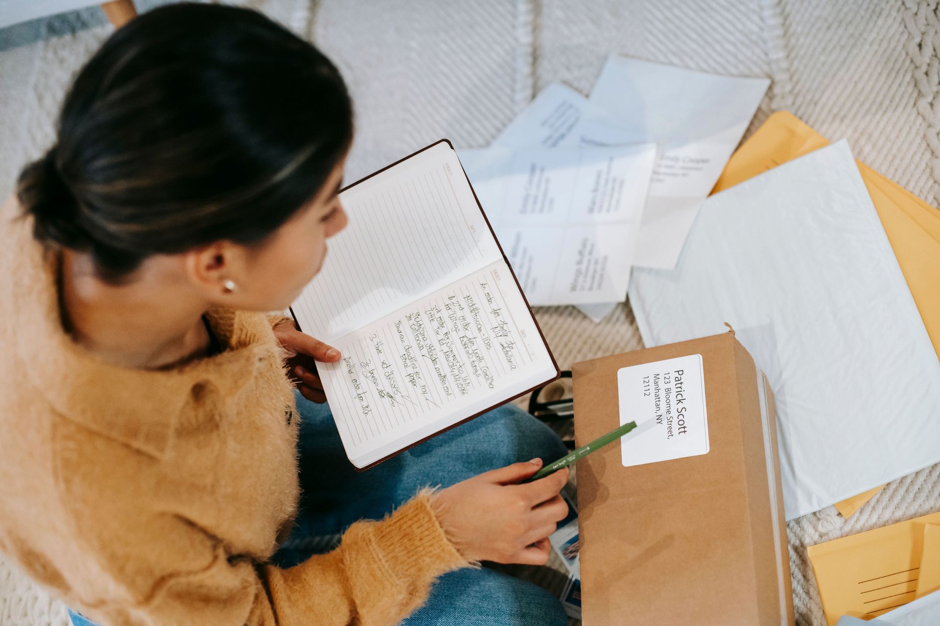 Person sorting papers and writing in a notebook at a desk with scattered documents and envelopes.