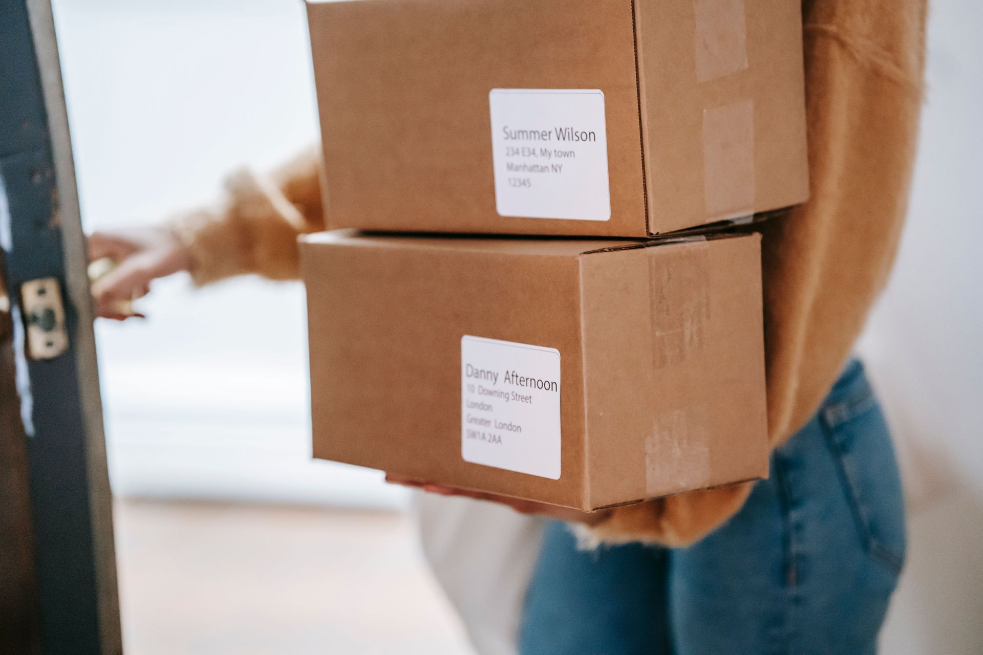 Person carrying two stacked cardboard boxes at a doorway