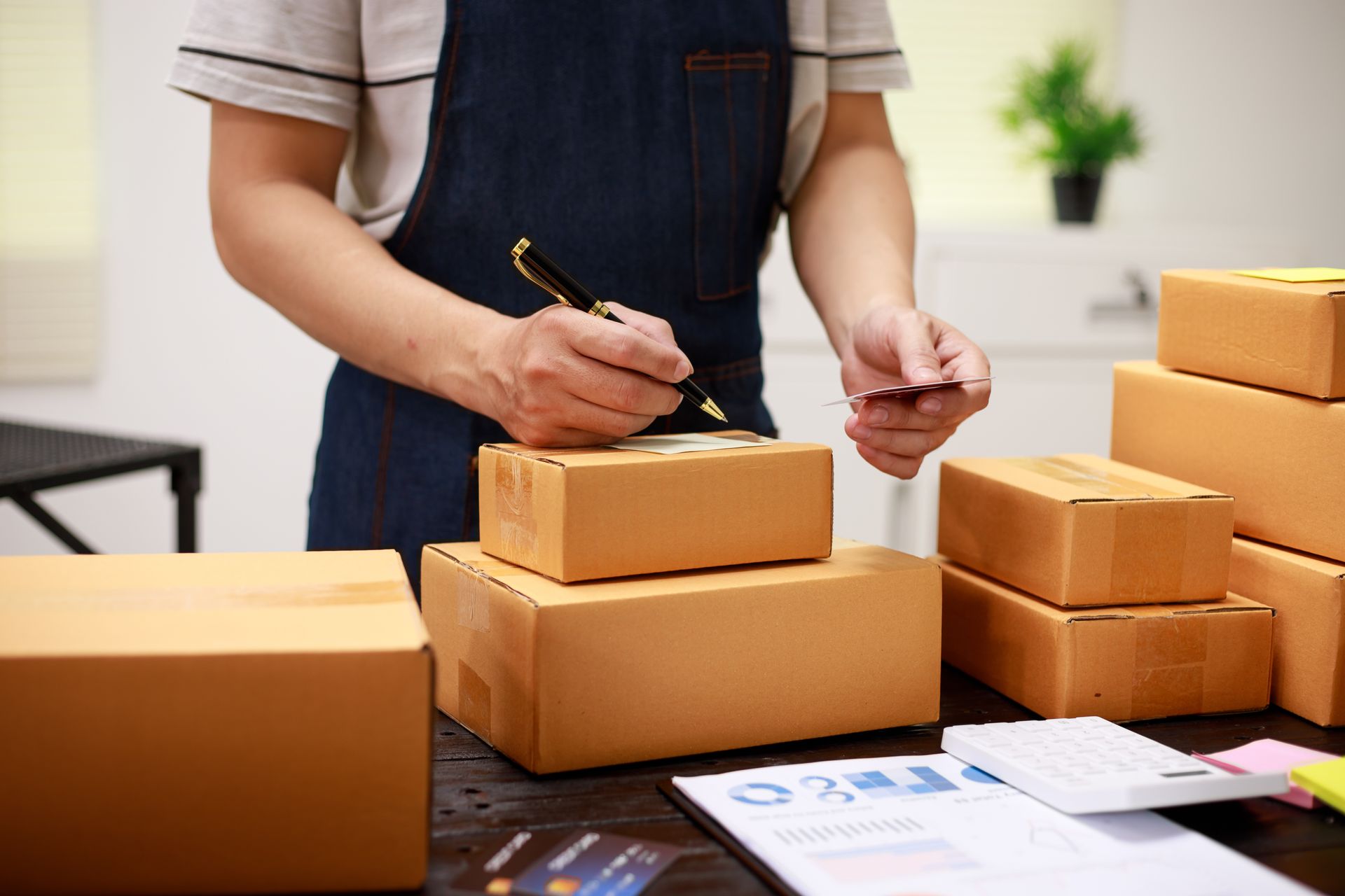 Person signing a credit card while surrounded by shipping boxes.