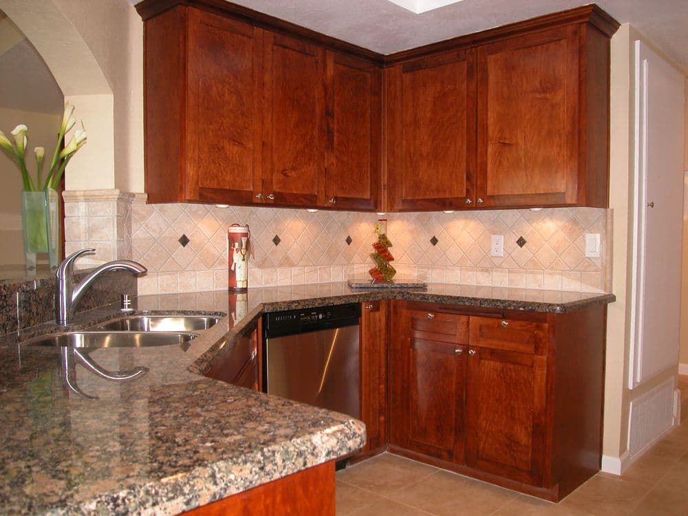 Kitchen corner with dark wood cabinets, granite countertops, stainless sink, and tiled backsplash.