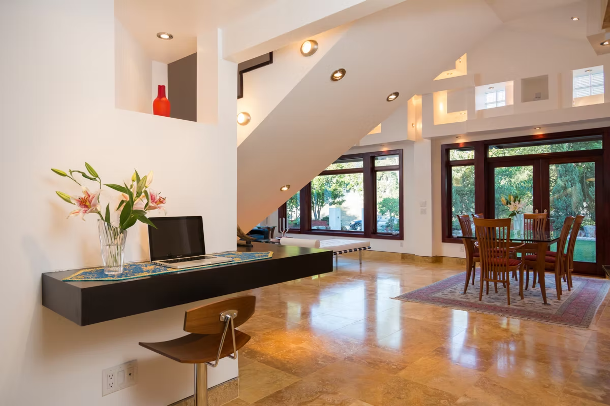 Modern open living room with stairs, hardwood floors, dining table, and large windows letting in natural light