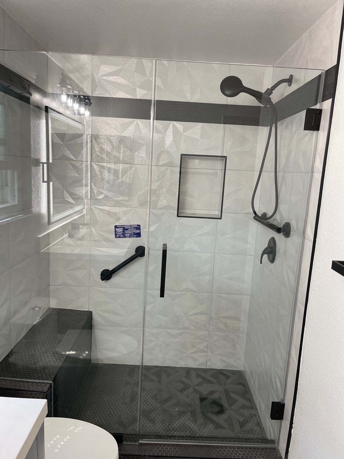 Accessible shower with folding bench, grab bars, handheld shower, and black non-slip floor tiles.