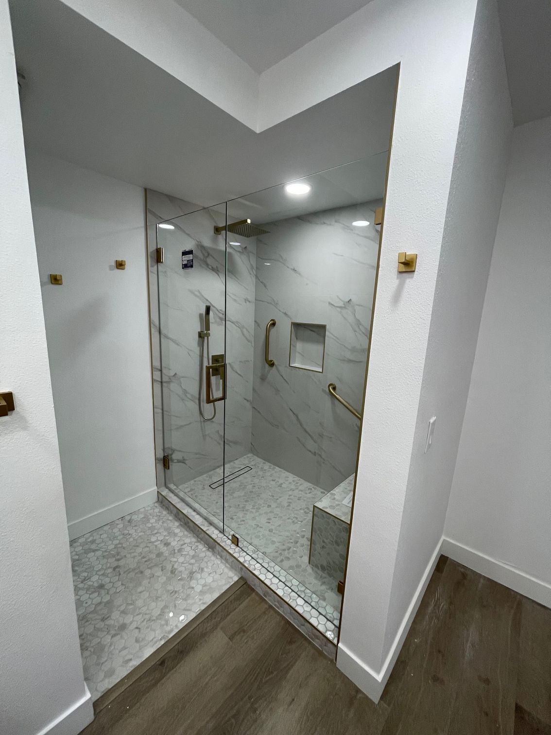Modern bathroom with glass-enclosed shower, gray tile, and wood-look floor in a bright white space